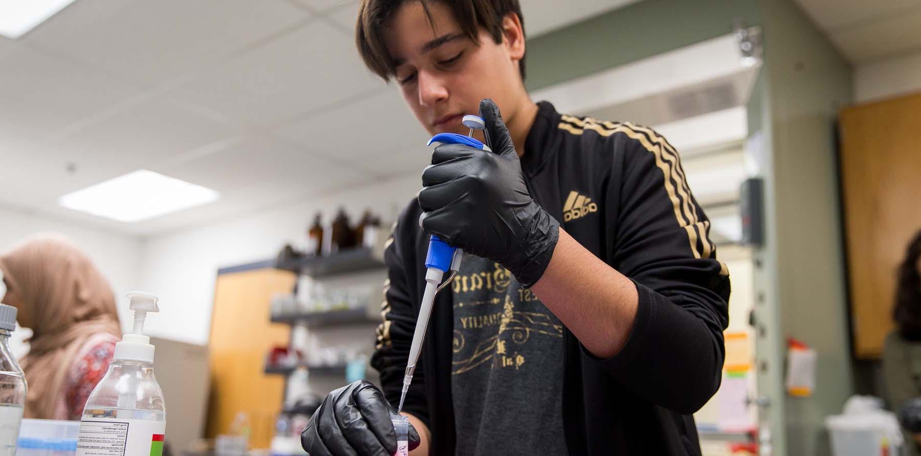 A Frontiers of Science Institute student titrates a solution into a test tube.